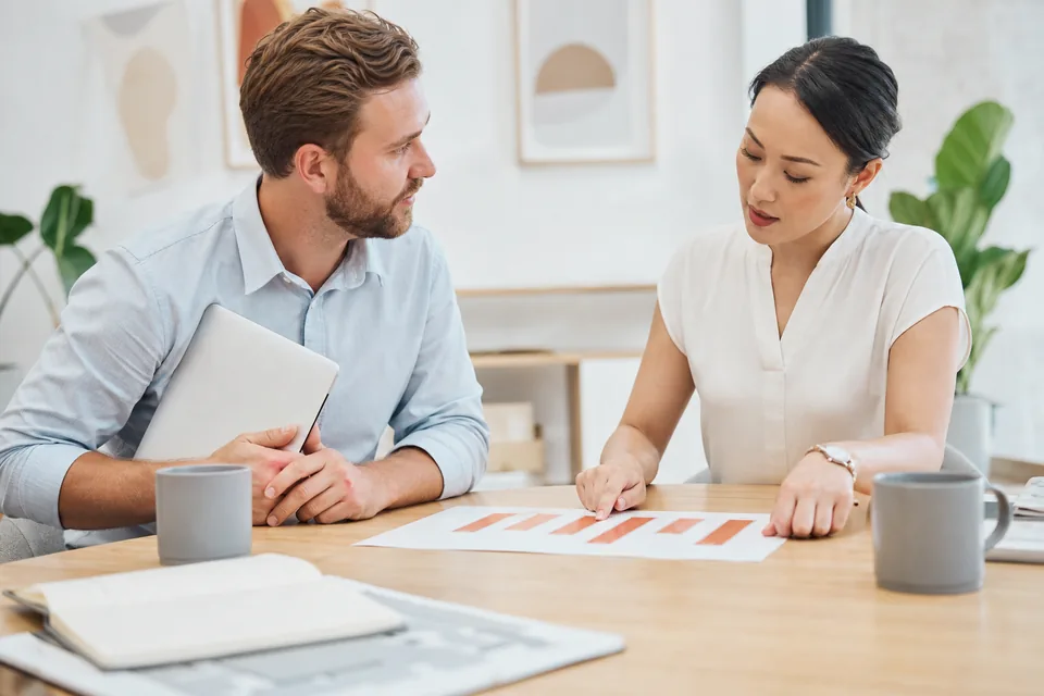 Two agency colleagues discussing a client budget chart at a meeting table